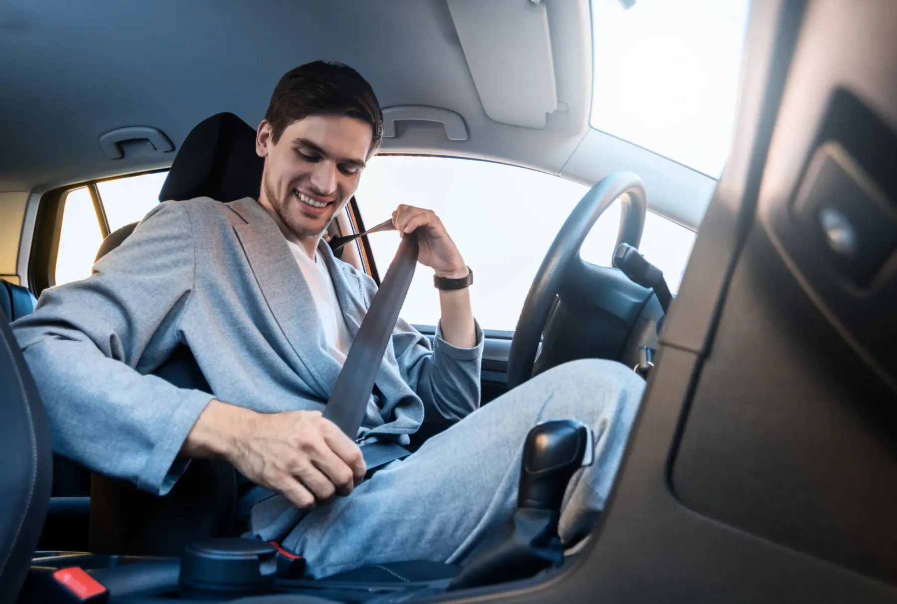 A driver seated in a car cabin drawing the three-point seat belt across the chest before fastening it