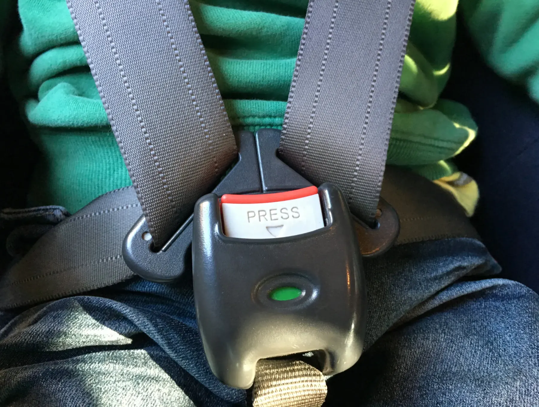 A secured harness-style seat belt buckle with a press release button holding two shoulder straps across a seated occupant